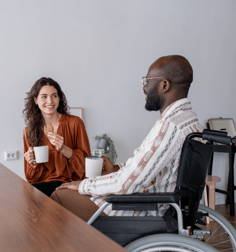 disability nurse with man in wheelchair at home talking and smiling
